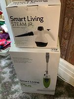 Boxes of Smart Living Steam Jr. hand steam cleaner and Steam Mop Plus stacked showing front and top sides.
