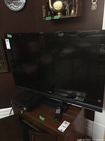 Full view of Sony Bravia 40-inch flat screen TV on wooden stand with remote and black device below