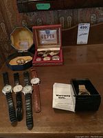 Overview of four leather-strap watches on table, digital watch in black case, Bulova and Gruen boxes in background