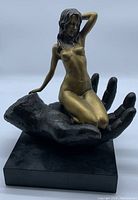 Front three-quarter view of bronze female figure kneeling in hand on marble base