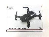 Top view of the drone displayed on the product box showing the foldable arms and integrated camera lens.