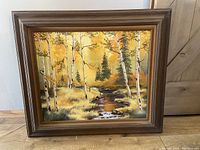 Framed landscape painting with yellow and brown autumn colors, birch trees, and a clear stream.