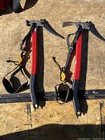 Pair of red Black Diamond ice axes with metal heads and attached wrist leashes shown on a wooden surface.