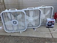 Three white plastic box fans arranged side by side, showing used condition.