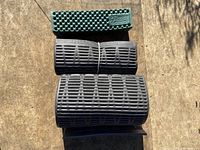 Top view of three rolled and bound sleeping pads stacked together, showing one green textured Therm-a-Rest pad and two black ribbed foam pads.