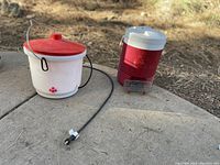 Photo showing two manual chicken waterers and one electric waterer on ground outdoors
