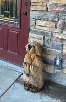 Wooden dog carving leaning against a stone wall near a front door, showing overall size and condition.