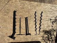 Several black metal grid wall hanger accessories arranged on a flat surface showing different styles including vertical arms with hooks and smaller hook attachments.