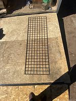 Single black metal gridwall panel with square grid pattern laid flat on plywood surface.