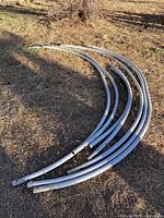 Four curved metal poles for hoop house arches lying on grass outdoors