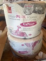 Photo showing two rolls of Owens Corning Ecotouch Pink attic insulation wrapped in clear plastic, labeled as unfaced and new.