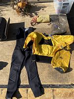 Photo showing wetsuit, yellow waterproof jacket, dry bag, and rescue rope storage on a wooden surface.