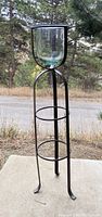 Full view of the black metal candle stand outdoors showing its tripod base and glass container.