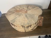 Top-down view of a large sanded wood log slice with natural wood grain and a branch stub visible.