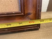 Close-up of bottom corner of wooden frame with tape measure showing the width of approximately 33 inches.