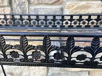 Close-up photo of the decorative floral and leaf pattern on the side of the black metal plant stand.