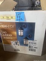 Box packaging showing two outdoor lanterns with product image depicting one style of lantern with bronze finish and frosted glass.