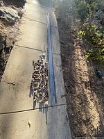 Assortment of galvanized pipe fittings and several galvanized pipes laid out on concrete