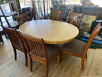 Photo of oval wooden dining table with six matching chairs arranged around it. Shows table top and chair upholstery.