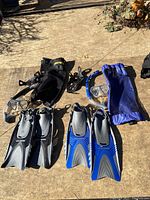 Full view of both snorkeling sets laid out on ground showing fins, masks, snorkels, and carry bags.