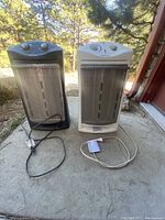 Two upright Holmes space heaters, black and white, showing front and controls, with cords laid out