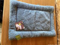 Full view of blue plush pet bed with bolstered edges and tag attached, placed on wooden surface.