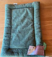 Photo of the green rectangular pet bed with a raised edge on a wooden floor, showing texture and size.