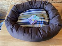 Full view of brown bumper pet bed with green, blue, and white striped cushion on top, tags visible