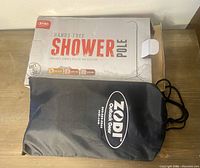 Photo of the Zodi branded black nylon storage bag with the original packaging box labeled 'Hands-Free Shower Pole'