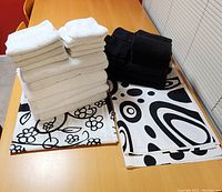 Image of stacked white and black towels and washcloths alongside folded retro-patterned black and white shower curtains on a wooden table.