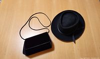 Photo showing the black felt hat and black velvet purse placed on a surface side by side.