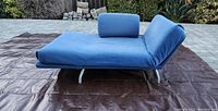Side view of blue adjustable lounge chair in flat bed configuration outdoors with brown tarp underneath.
