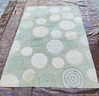 Full view of CB2 green circles rug with visible stains and pattern details on a brown tarp.