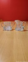 Front view of crystal sugar bowl and cream pitcher on wood table with red background
