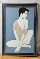 Front view of framed serigraph print depicting seated woman in beige top, blue background, signed in lower right.