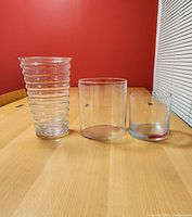 Three glass cylinder vases on a wooden table against a red wall, showing varying shapes and sizes.