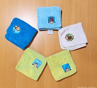 Five terrycloth washcloths arranged on a wooden surface showing monkey appliques. Includes blue, light blue, white, and green colored washcloths with some staining and discoloration visible.