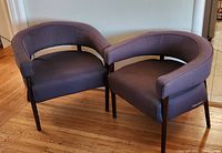 Pair of dark brown upholstered mid-century modern chairs with curved wooden arms and legs on hardwood floor.