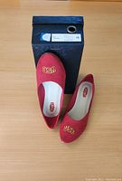 Photo showing the pair of red USC ballet flats placed on and next to their original black shoe box labeled size 10.