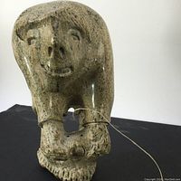 Front view of the Eskimo hunter stone sculpture showing detailed facial features, bent forward posture, and attached line.