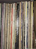 Collection of LP vinyl records showing a variety of artist names and titles, with visible wear on sleeves and tape labels from a radio station.