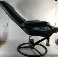 Side view of the green leatherette lounge chair showing reclining backrest and padded armrests over black steel tube frame with circular base.