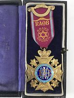 Front of RAOB Grand Council Medal showing maroon ribbon with gold bar and detailed star shaped medal with crown and blue enamel.