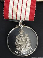 Front view of the medal showing the Canadian coat of arms and the years 1867-1967 with attached red and white striped ribbon.