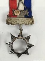 Close-up photo of 1931 Lodge Royal Rose medal showing star-shaped pendant, floral design, and red, white, blue ribbon with engraved plate.