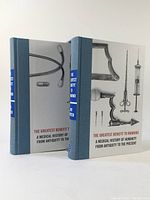 Front and back angled view of the two volumes showing the illustrated dust jackets with vintage medical instruments and blue cloth spines.