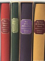 Front view showing the spines of four Thomas Hardy novels in different colored cloth bindings with gold embossing and their slipcases.