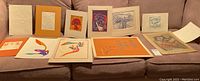 Group of ten assorted prints and drawings laid out on a sofa