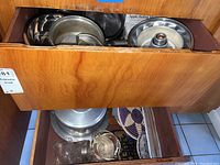 Drawer with metal Bundt pans, mixing bowls, apple peeling machine lid, and glass items beneath.