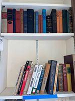 Wide view of two bookshelves with a variety of hardcover books showing different sizes and cover colors, some titles readable.